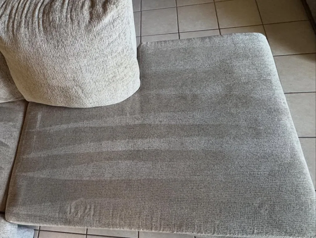 The same light fabric sofa cushion after cleaning, with even pile and visible extraction lines across the seat.